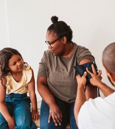 Mother talking with daughter while doctor measuring blood pressure